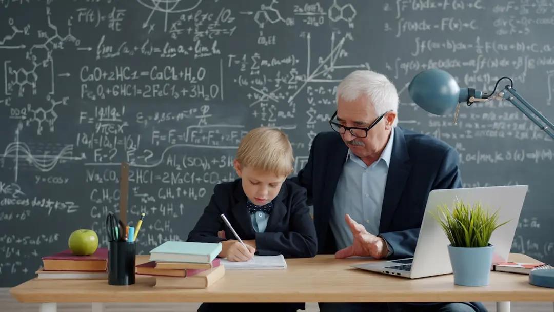 A teacher sitting beside a student, working through a math problem together at a desk