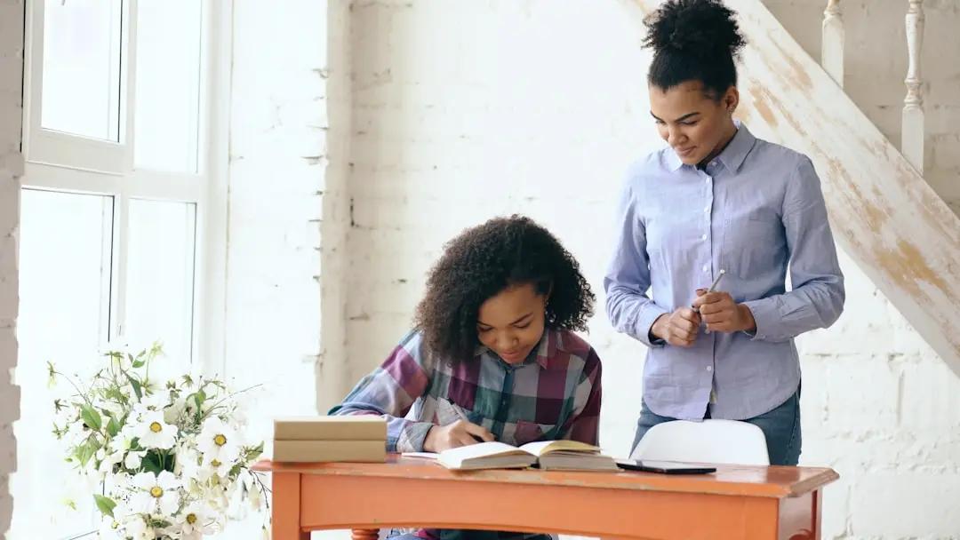 A teacher kneeling beside a student's desk during a one-on-one check-in