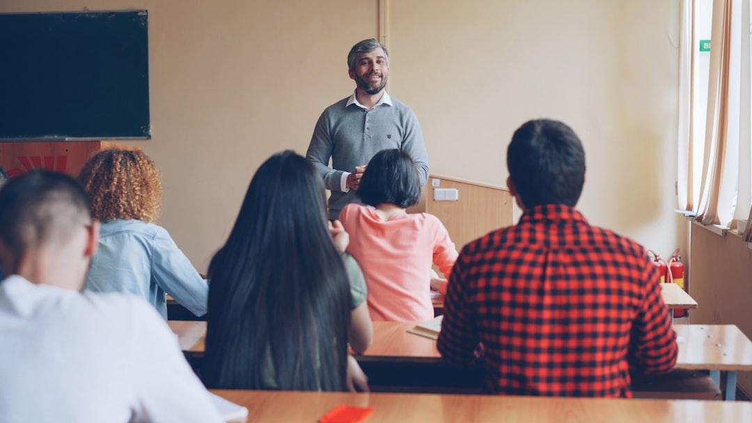 A teacher standing at the front of a classroom while students at desks listen and take notes