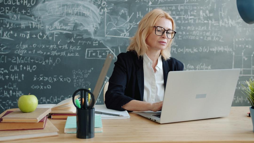 Teacher working on a laptop in front of a classroom chalkboard